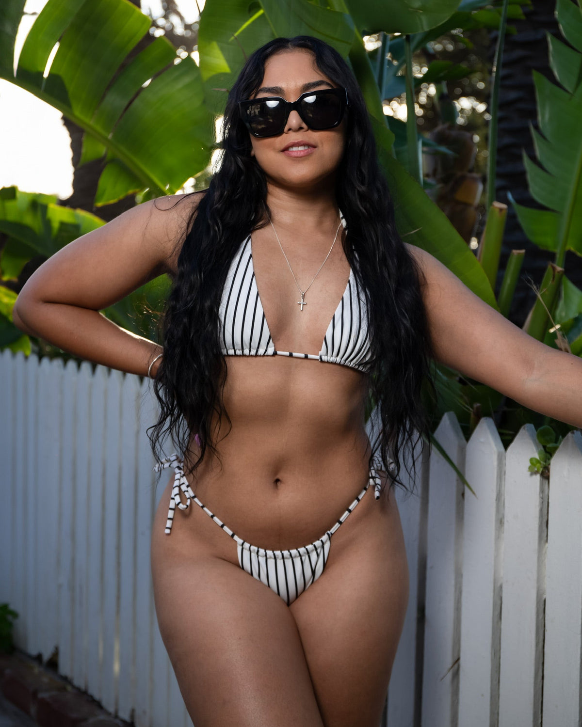 This image features a stylish Cabo Bikini Bottom in a mono, or single-color, variant. The model is showcased wearing the bikini bottom along with a matching top, posing confidently against a lush, green backdrop.