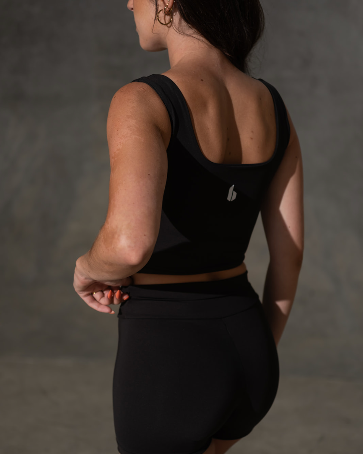 Person wearing a black athletic outfit with a logo on a plain background