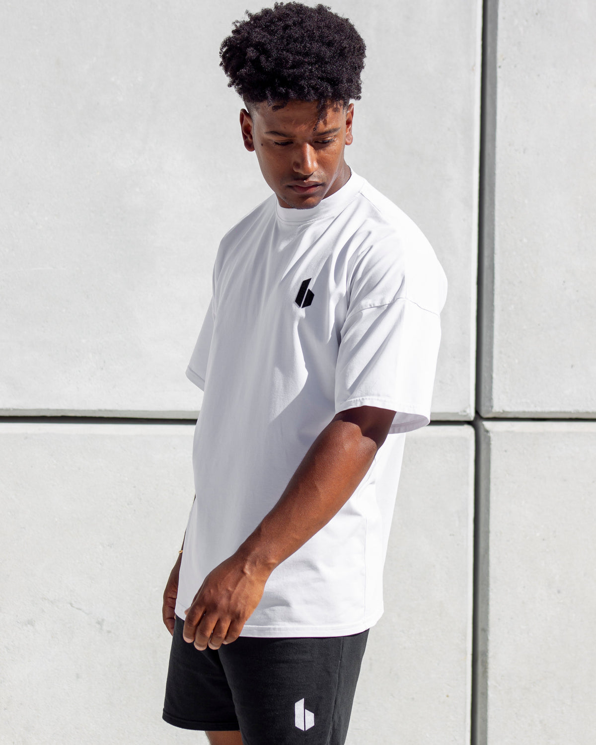 A man wearing a white oversized T-shirt with a logo on the chest and black shorts.