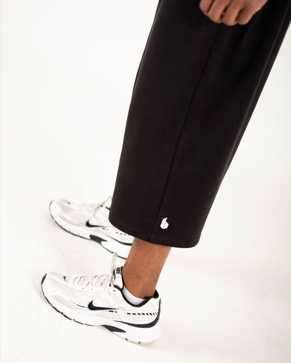 A close-up of a person's lower legs wearing black sweatpants and white Nike sneakers with black swooshes, set against a clean white background.