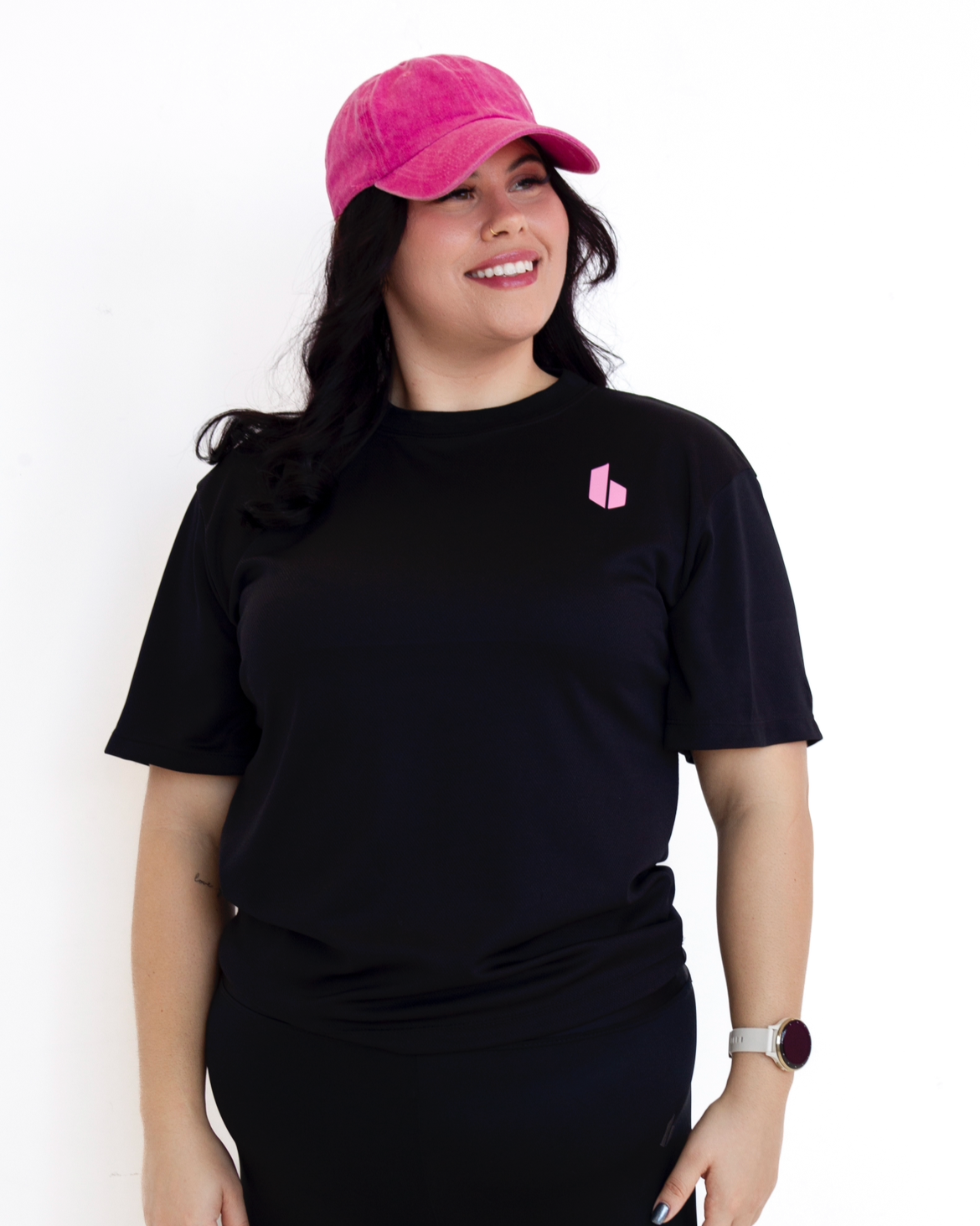 Person wearing a black t-shirt with a logo and a pink cap on a white background