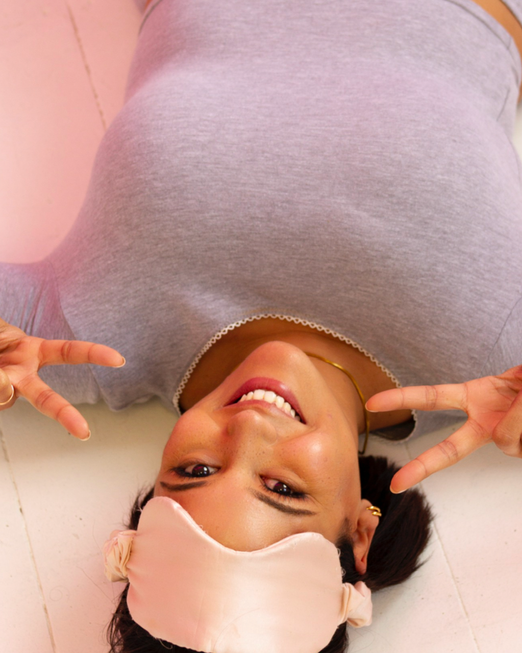 Person wearing a face mask and gray sweater, upside down on a light pink floor.