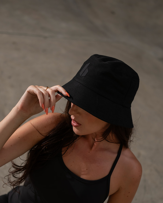 Woman wearing a black hat and black top sitting on a concrete surface.