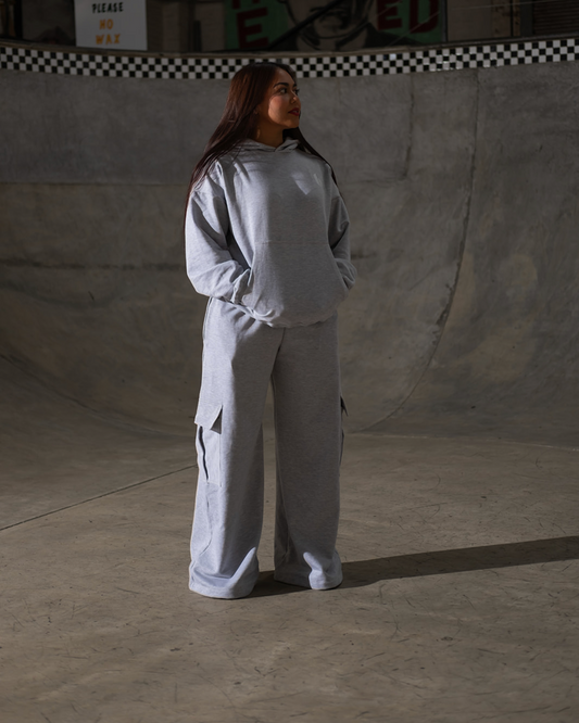 Person wearing a gray tracksuit in an indoor skate park with graffiti on the wall.