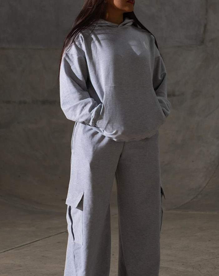 Person wearing a gray tracksuit in an indoor skate park with graffiti on the wall.