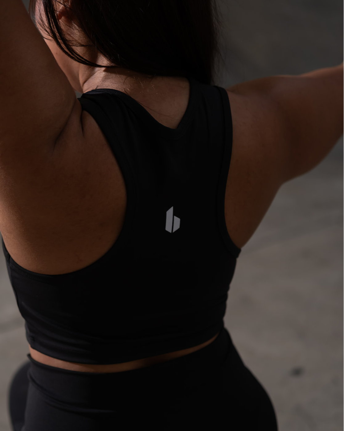 Person wearing a black sports bra with a logo, standing against a neutral background