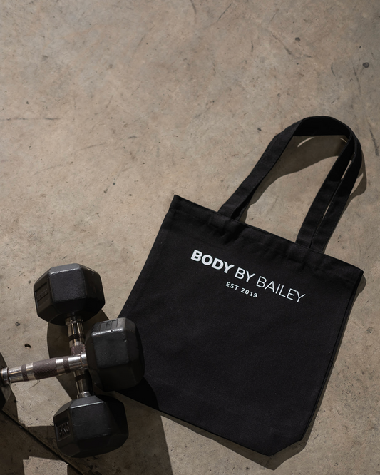 Black tote bag with 'Body by Bailey' branding on a concrete surface.
